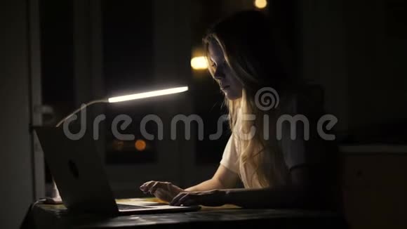 使用笔记本电脑的女学生在黑暗房间接受在线教育视频的预览图