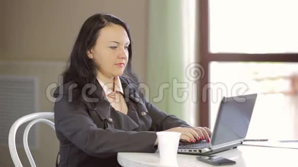穿着深色夹克的年轻女人在笔记本电脑上工作喝咖啡慢点视频的预览图