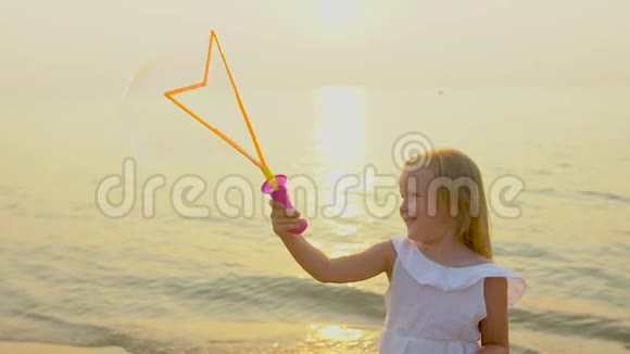 快乐可爱的小女孩在美丽的夕阳下在海滩上玩肥皂泡在缓慢的假期里快乐的度假视频的预览图