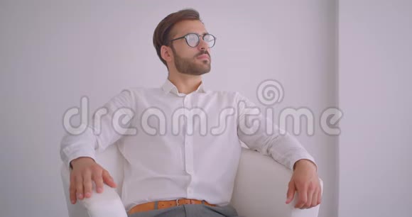 一位成年英俊的白种人白种人商人坐在白色办公室的扶手椅上的特写画像视频的预览图