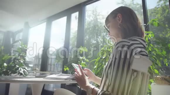 Brunette女士独自一人在一家有全景窗户的咖啡馆里使用智能手机视频的预览图