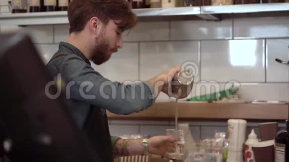 年轻的男咖啡师准备奶昔并倒入塑料杯视频的预览图