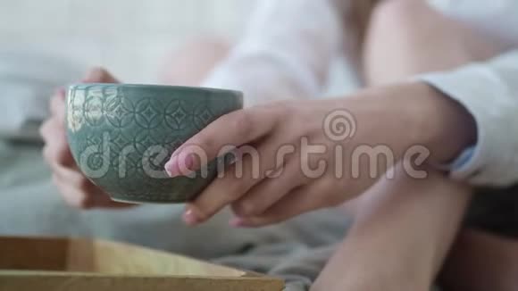 美丽的女孩坐在床上喝着茶看着相机微笑着相机在杯子后面移动视频的预览图