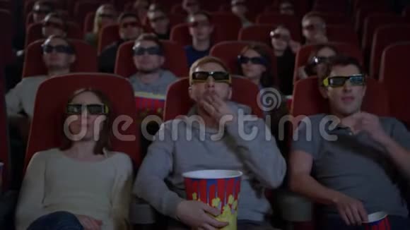 坐在电影院看3D电影和吃爆米花的年轻人视频的预览图