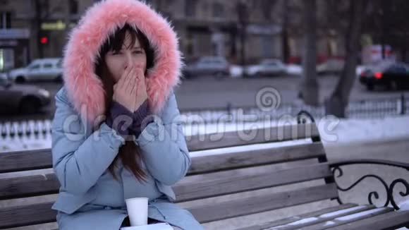 冬天一个穿灰色外套的女孩试图在街上温暖她冻僵的手视频的预览图