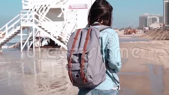 带背包的女人在海岸警卫队哨所附近散步头发随风飘动女孩在海边散步慢动作视频的预览图