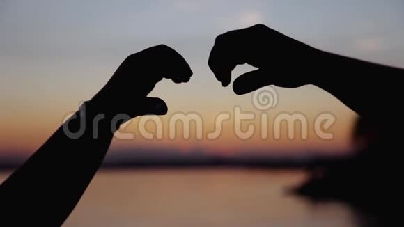 年轻的一对情侣在沙滩上迎着金色的夕阳亲吻做着心形图案视频的预览图