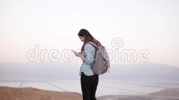 女人使用智能手机近黄昏蒙丹风景慢动作休闲女孩与背包类型在信使应用程序以色列视频的预览图