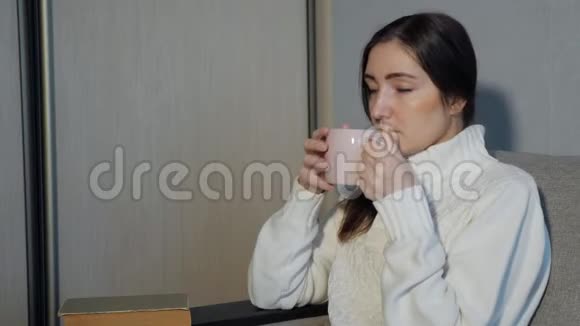 美丽的女孩喝茶在沙发上看书视频的预览图