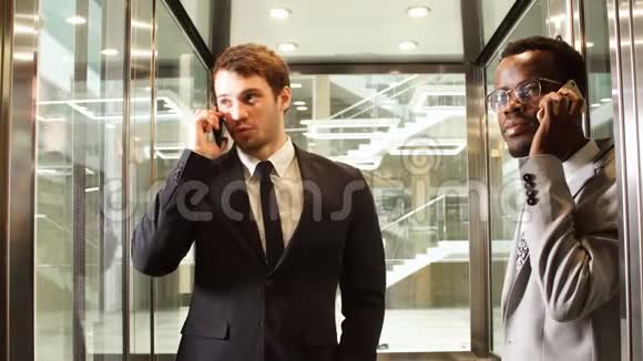 两名跨国商务人员站在电梯里使用智能手机大型玻璃电梯里的商务人士视频的预览图