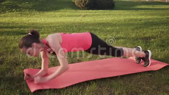 健身妇女在草地上做动态木板运动阳光明媚的夏日视频的预览图