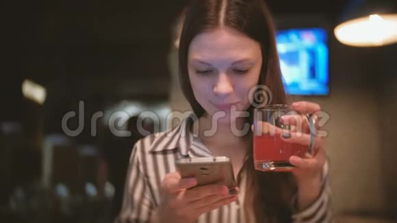 年轻漂亮的黑发女人在手机里看东西微笑着在咖啡馆里喝红凉茶视频的预览图