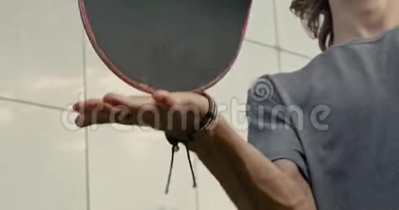 一个年轻的卷发男子的特写镜头他在手中缓慢地转动滑板视频的预览图