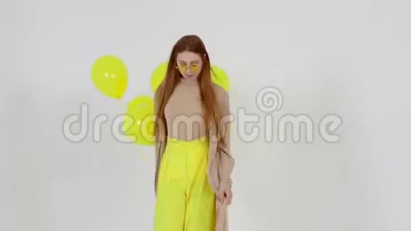 穿着黄色裙子手里拿着黄色气球的女孩正在灯光背景下对着相机摆姿势视频的预览图