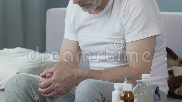 沮丧的老年男性坐在床上瓶子和药品站在附近视频的预览图