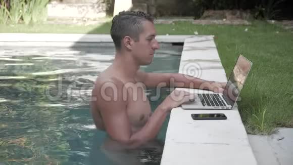 坐在游泳池里用笔记本电脑工作的商人那个自由职业者在度假村一个漂亮的地方工作视频的预览图