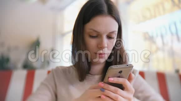 年轻漂亮的黑发女人在咖啡馆里用手机打字和发送信息等待她的朋友视频的预览图