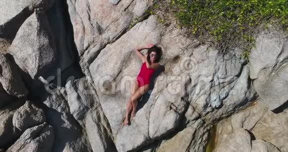 空中美丽的女孩穿着红色比基尼躺在石头上摆姿势视频的预览图