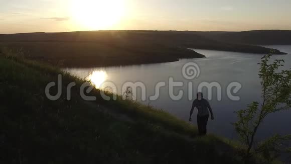 空中史诗拍摄的一个人徒步在河岸边作为一个轮廓在美丽的日落视频的预览图