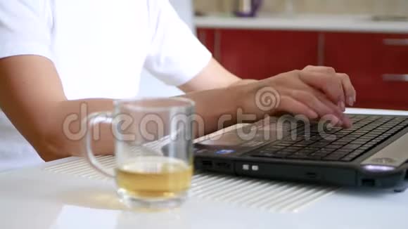手的女孩在笔记本电脑的键盘上打字笔记本电脑旁边是一杯茶视频的预览图