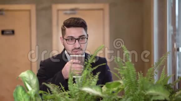 戴眼镜的黑发年轻人喝咖啡视频的预览图