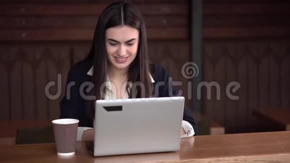 在咖啡馆里一个笑容满面的黑发女孩在手提电脑上打字紧握着拳头喝着咖啡她很高兴视频的预览图