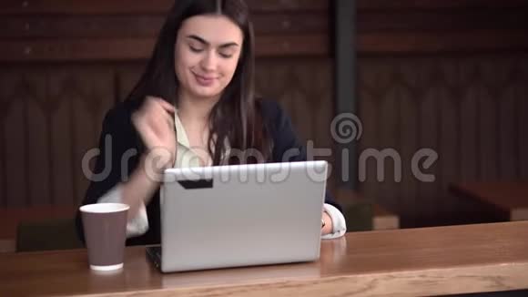 一个拿着笔记本电脑和咖啡的布鲁内特女孩在做一个重要的决定之前想了想挥手表示她是视频的预览图
