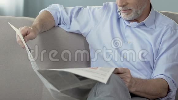 大胡子老人坐在沙发上看报纸周末早间新闻视频的预览图