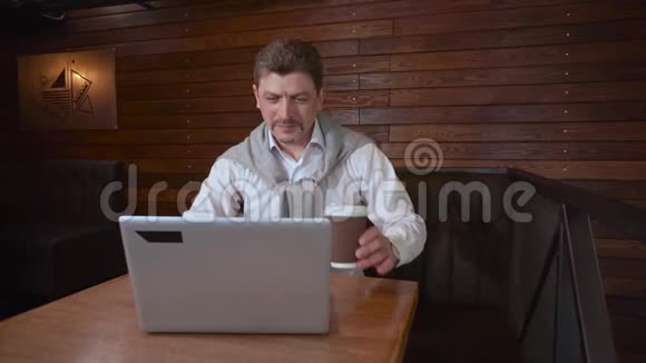 咖啡屋里的成年帅哥喝着咖啡微笑着合上笔记本电脑开始跳舞展示了这项工作的成功视频的预览图