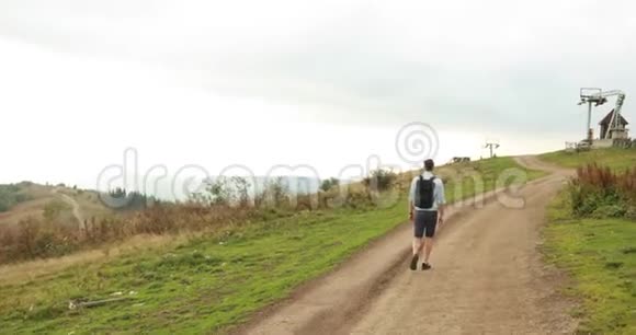 孤独在山里英俊的年轻人背着背包在灰色的天空下沿着山路散步视频的预览图