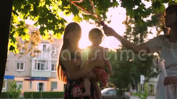 妈妈和小女儿在城市公园里捉到又大又透明的肥皂泡笑起来视频的预览图