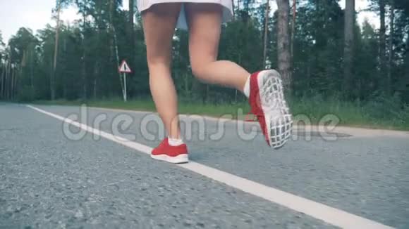 穿着运动鞋的年轻女士正在沿着森林公园缓慢地奔跑女运动员慢跑视频的预览图