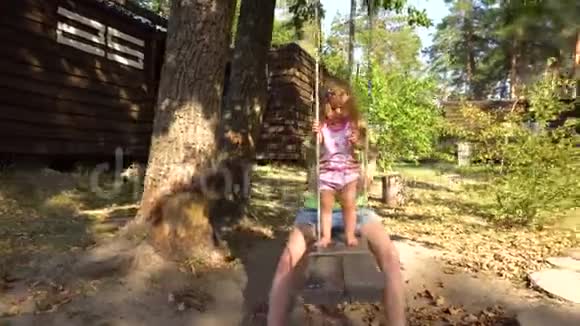 带着女孩坐在树下的木跷跷板上视频的预览图