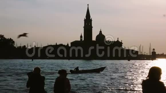 人们坐在运河上的威尼斯欣赏日落的剪影男性拍摄风景视频的预览图