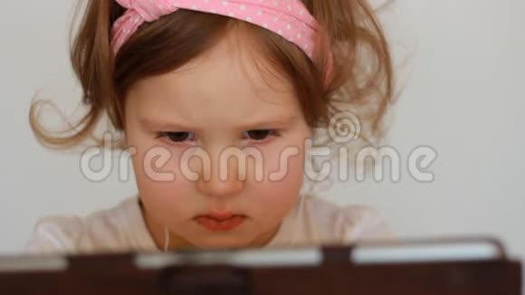 一个戴着耳机的小可爱女孩看着屏幕监视器平板电脑看电视录像卡通或玩游戏的滑稽儿童视频的预览图