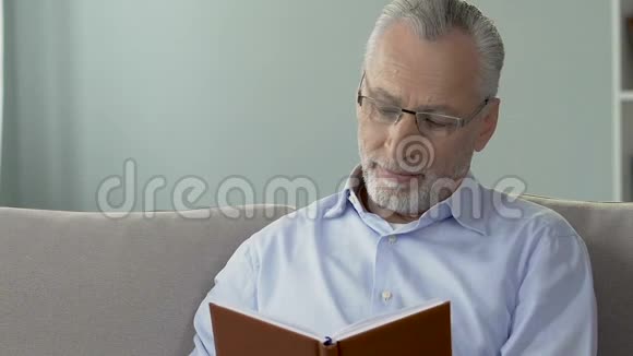老年男性坐在沙发上看书退休后娱乐时间视频的预览图