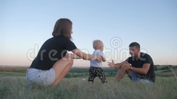 小男孩在爸爸妈妈的帮助下迈出了他的第一步户外生活方式概念家庭视频的预览图