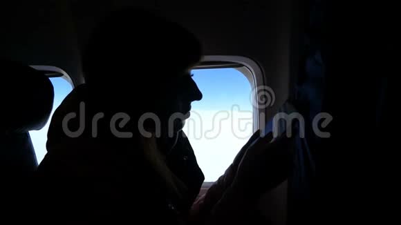 在飞机的机舱里女孩黑暗的轮廓在智能手机上阅读一些东西对抗着视频的预览图