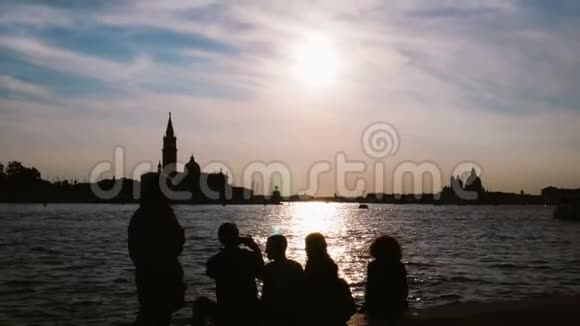 一群年轻人坐在威尼斯的频道里欣赏日落视频的预览图