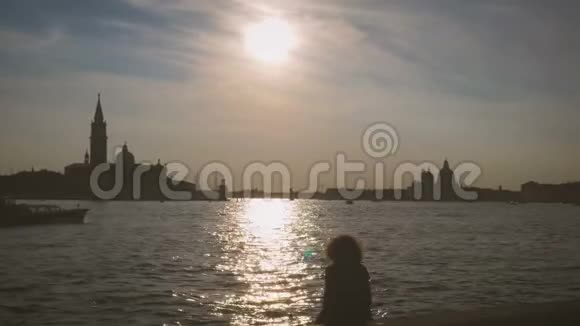 坐在威尼斯的女孩坐在运河上坐着漂浮的小船欣赏日落视频的预览图