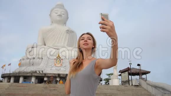 慢动作模特年轻女士在泰国佛像附近的智能手机上自拍视频的预览图