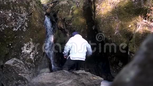 一个穿着白色夹克的人在峡谷的瀑布下的后景录像站着的游客视频的预览图