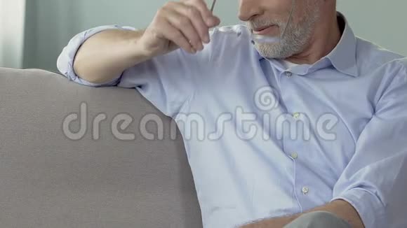 老年男性摘下眼镜触摸胡须回忆过去特写视频的预览图