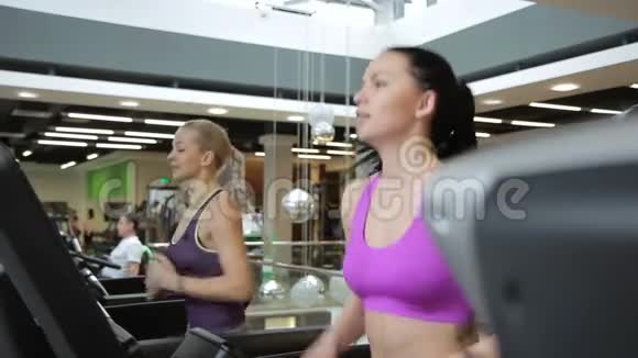 两个漂亮的女人在跑步机上跑步在宽敞的健身房里交谈视频的预览图