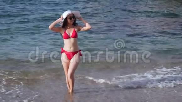 穿着红色泳装的女人站在海滩上的水里视频的预览图