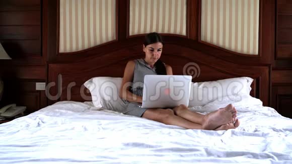 年轻女子坐在床上用笔记本电脑工作4k视频的预览图