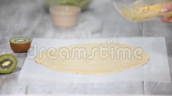 女性的手在生面团上涂上奶油用新鲜的猕猴桃做小面包视频的预览图