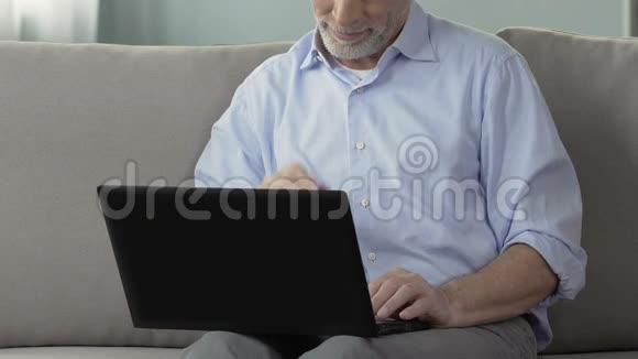 老人坐在沙发上使用笔记本电脑在家工作工程项目视频的预览图