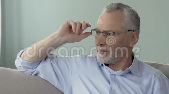 戴眼镜的高年级男坐在沙发上侧着头看着深深地想着视频的预览图