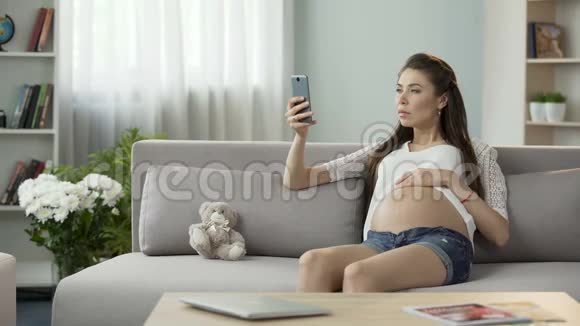 女性怀孕孩子坐在沙发上使用手机在线博客视频的预览图